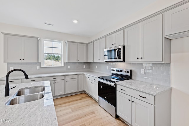 kitchen featuring sink, tasteful backsplash, appliances with stainless steel finishes, light stone countertops, and light hardwood / wood-style floors