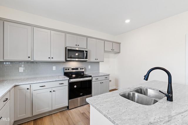 kitchen featuring appliances with stainless steel finishes, sink, light stone counters, and light hardwood / wood-style flooring