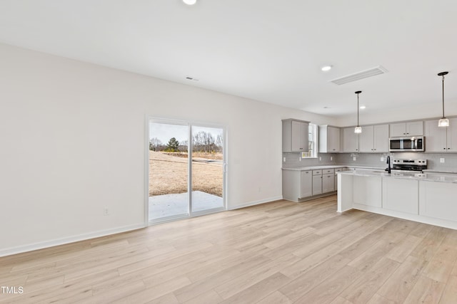 kitchen featuring gray cabinets, pendant lighting, stainless steel appliances, light hardwood / wood-style floors, and backsplash