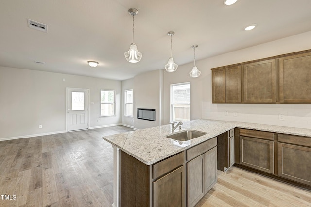 kitchen featuring decorative light fixtures, light stone countertops, sink, and light hardwood / wood-style flooring