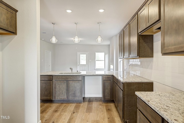 kitchen featuring sink, backsplash, hanging light fixtures, light hardwood / wood-style floors, and light stone countertops