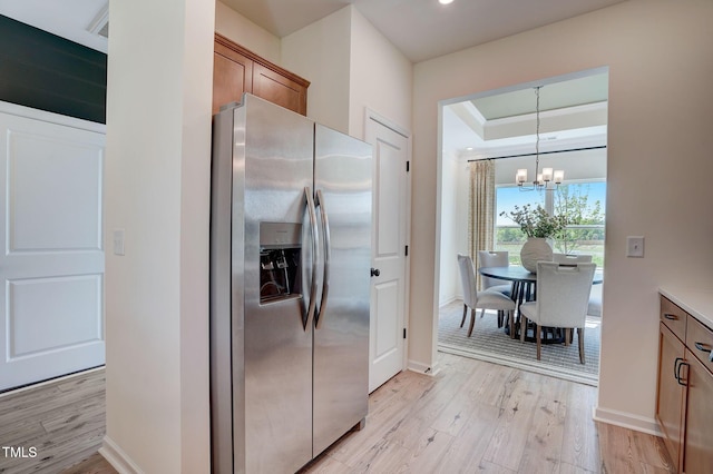 kitchen featuring an inviting chandelier, decorative light fixtures, light wood-type flooring, stainless steel fridge, and a raised ceiling