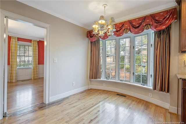 unfurnished dining area with a notable chandelier, crown molding, and light wood-type flooring