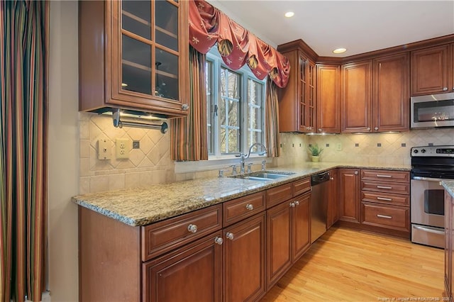 kitchen featuring tasteful backsplash, sink, light hardwood / wood-style floors, stainless steel appliances, and light stone countertops