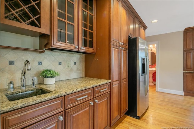 kitchen featuring stainless steel refrigerator with ice dispenser, sink, tasteful backsplash, light hardwood / wood-style flooring, and light stone countertops