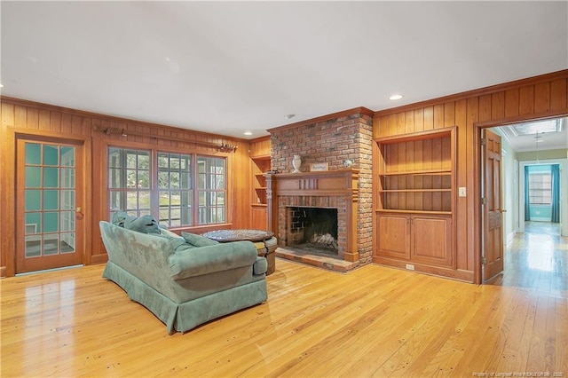 living room featuring wood walls, light hardwood / wood-style floors, crown molding, a brick fireplace, and built in shelves