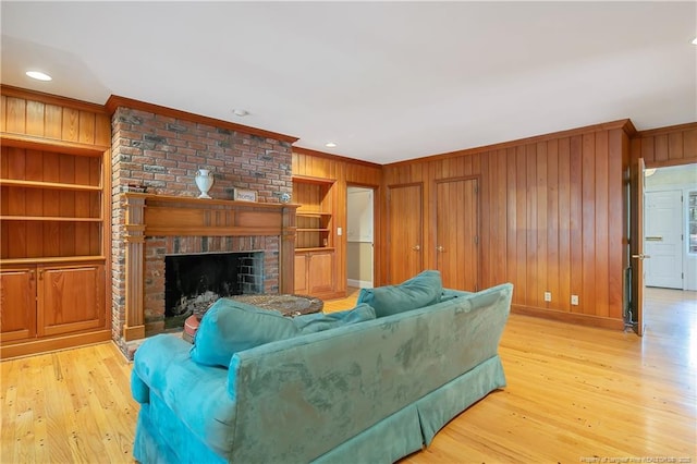 living room featuring built in shelves, ornamental molding, a fireplace, and light hardwood / wood-style floors