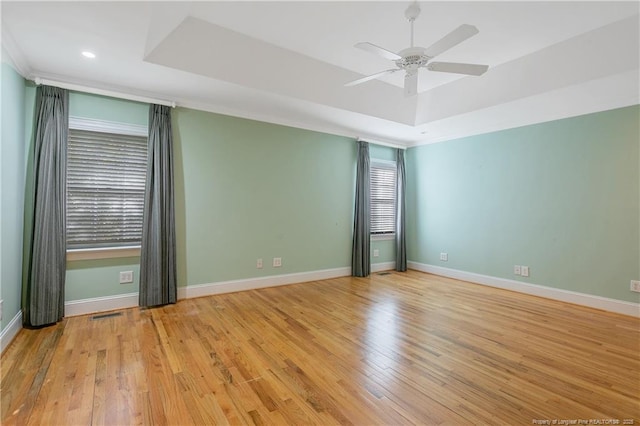 empty room featuring ceiling fan, a tray ceiling, and light wood-type flooring