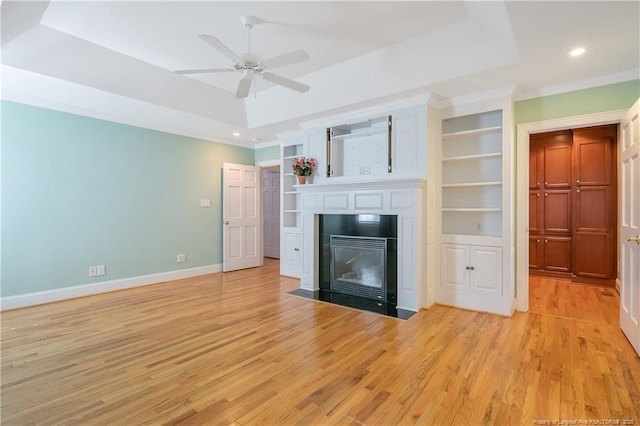 unfurnished living room featuring built in shelves, crown molding, a raised ceiling, and light hardwood / wood-style floors