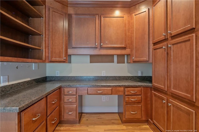 kitchen with dark stone countertops, built in desk, and light wood-type flooring