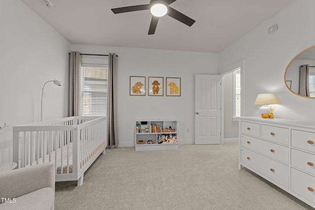 carpeted bedroom with ceiling fan and a crib