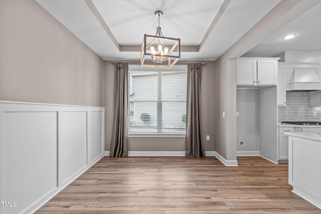 unfurnished dining area featuring a tray ceiling, light hardwood / wood-style floors, and a chandelier