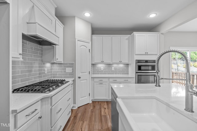 kitchen with sink, appliances with stainless steel finishes, light hardwood / wood-style floors, white cabinets, and custom exhaust hood