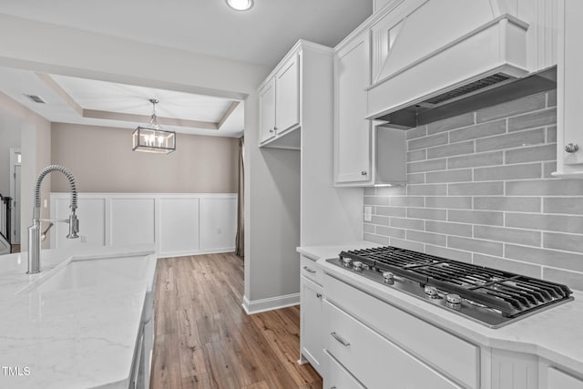 kitchen with stainless steel gas cooktop, sink, custom exhaust hood, a raised ceiling, and white cabinets