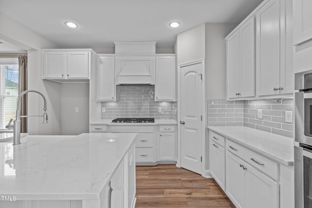 kitchen with appliances with stainless steel finishes, light stone countertops, custom exhaust hood, and white cabinets