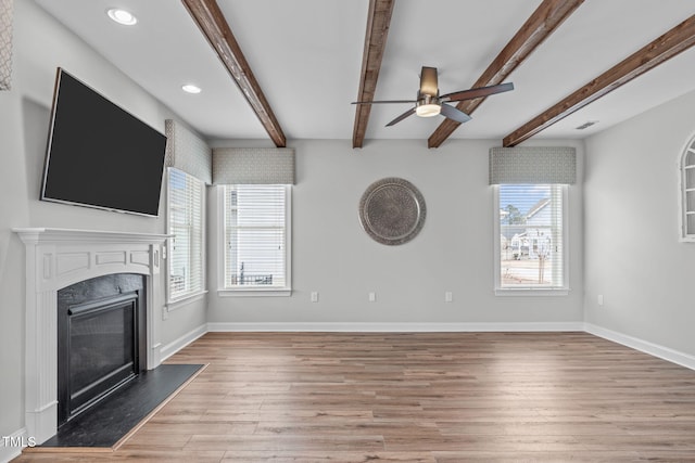 unfurnished living room with beam ceiling, ceiling fan, a high end fireplace, and light hardwood / wood-style flooring