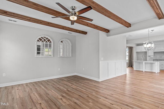 spare room featuring a healthy amount of sunlight, ceiling fan with notable chandelier, and light wood-type flooring