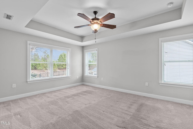 empty room with ceiling fan, a tray ceiling, and light carpet