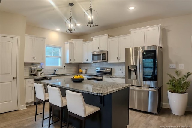 kitchen featuring sink, appliances with stainless steel finishes, a kitchen island, light stone countertops, and white cabinets