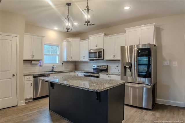 kitchen with sink, white cabinetry, appliances with stainless steel finishes, a kitchen island, and pendant lighting