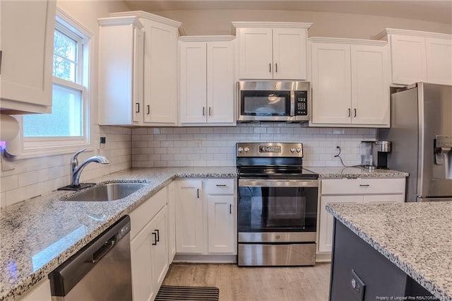 kitchen with sink, white cabinetry, light stone counters, light wood-type flooring, and stainless steel appliances