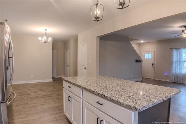 kitchen with white cabinetry, light stone counters, hanging light fixtures, stainless steel fridge, and a kitchen island