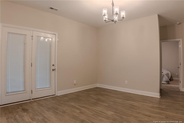 spare room featuring a notable chandelier and dark wood-type flooring