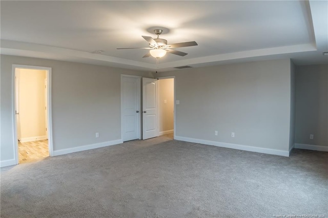 unfurnished room with a raised ceiling, light carpet, and ceiling fan