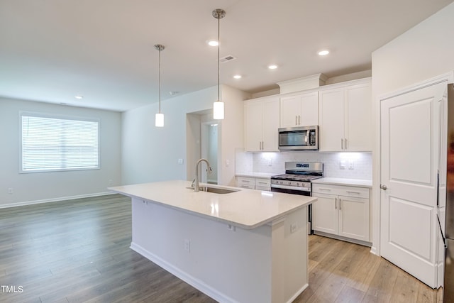 kitchen featuring hanging light fixtures, a center island with sink, white cabinets, and appliances with stainless steel finishes