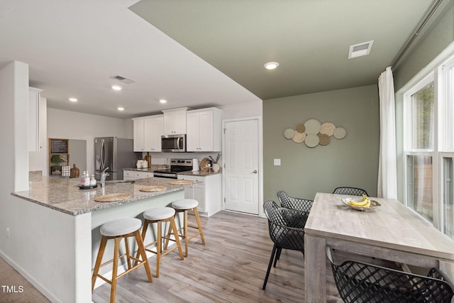 kitchen featuring appliances with stainless steel finishes, white cabinetry, a kitchen bar, kitchen peninsula, and light stone countertops