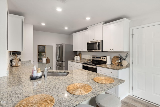 kitchen featuring white cabinetry, sink, kitchen peninsula, stainless steel appliances, and light stone countertops