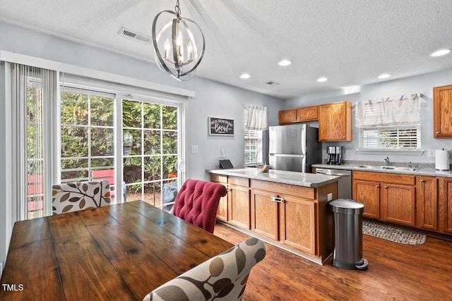 kitchen with sink, dark wood-type flooring, stainless steel appliances, light stone countertops, and decorative light fixtures