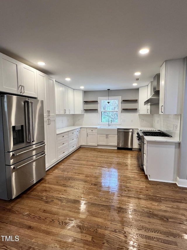 kitchen with white cabinetry, appliances with stainless steel finishes, wall chimney exhaust hood, and hanging light fixtures