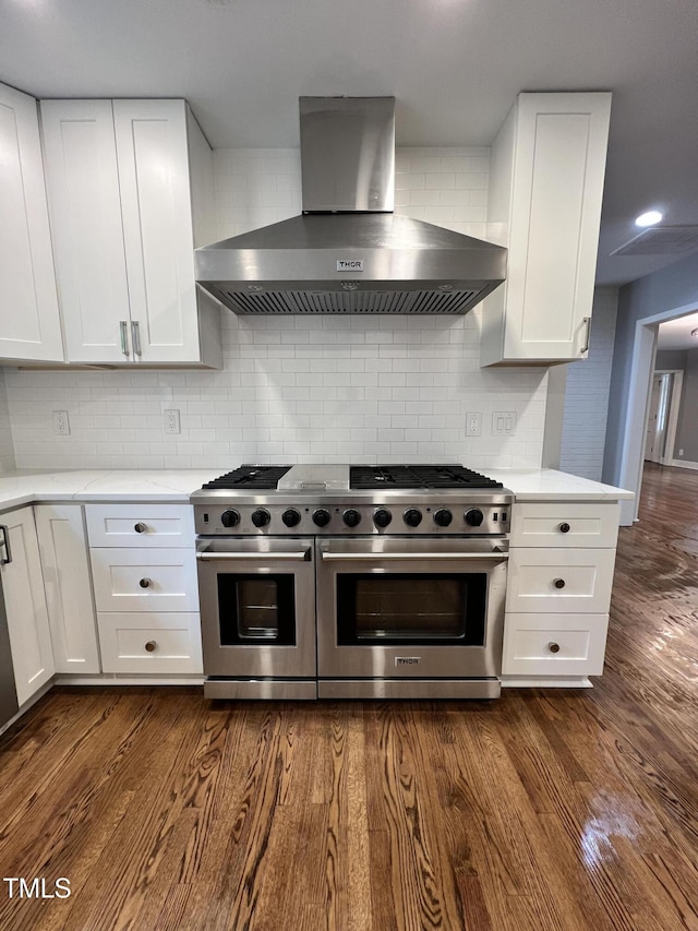 kitchen with white cabinets, stainless steel appliances, dark hardwood / wood-style floors, and wall chimney range hood