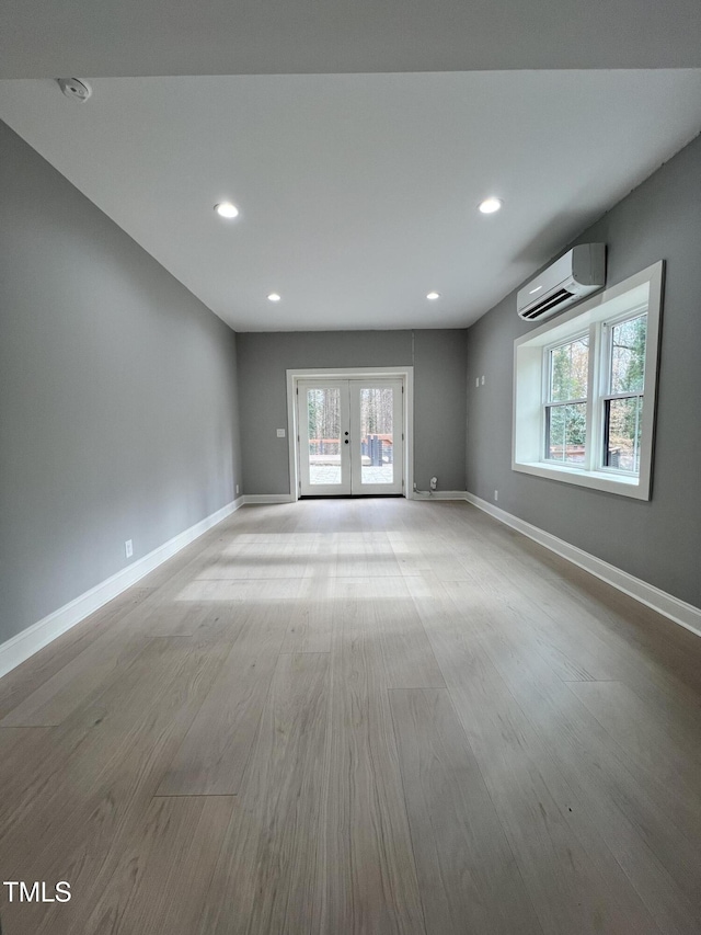 unfurnished room featuring a wall mounted air conditioner, light hardwood / wood-style floors, and french doors