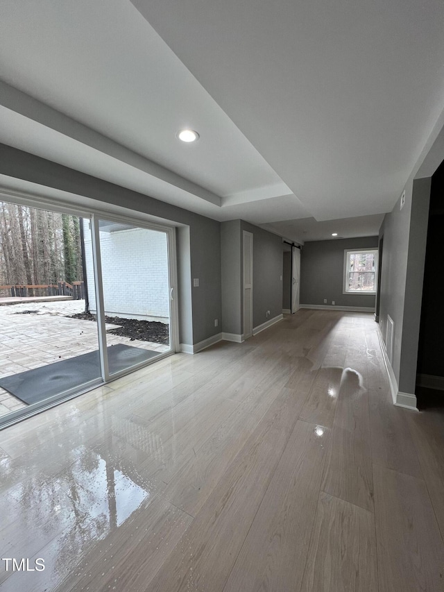 unfurnished living room featuring a barn door, a raised ceiling, and hardwood / wood-style floors