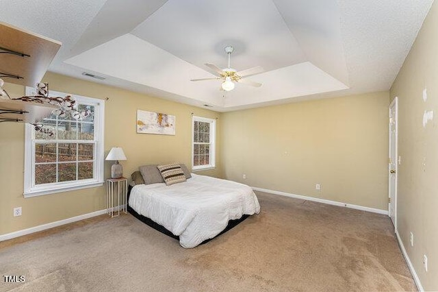 carpeted bedroom featuring ceiling fan and a tray ceiling