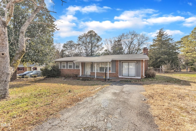 ranch-style house featuring driveway, covered porch, a chimney, a front lawn, and brick siding