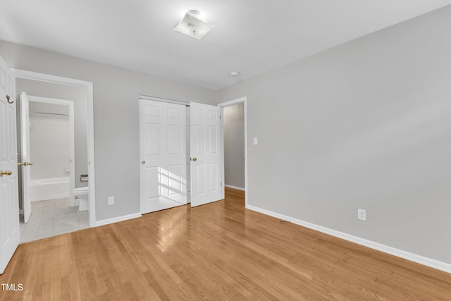 unfurnished bedroom with ensuite bath, a closet, and light wood-type flooring