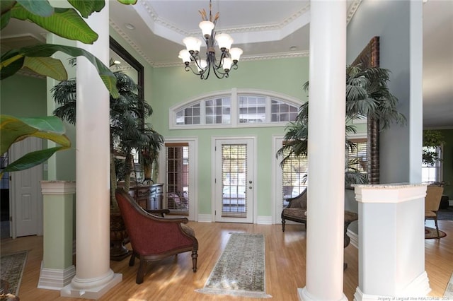 foyer featuring light hardwood / wood-style flooring, decorative columns, a high ceiling, a raised ceiling, and a chandelier