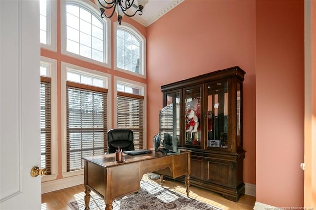 home office featuring a towering ceiling, a chandelier, and light hardwood / wood-style flooring