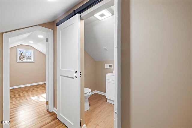 corridor featuring lofted ceiling, a barn door, and light wood-type flooring