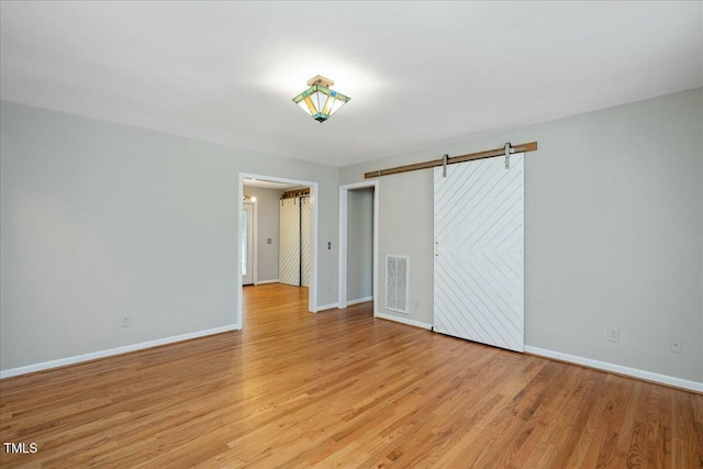 unfurnished bedroom with a barn door and light wood-type flooring