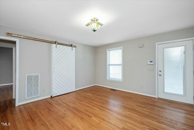 unfurnished room featuring a barn door and light hardwood / wood-style floors