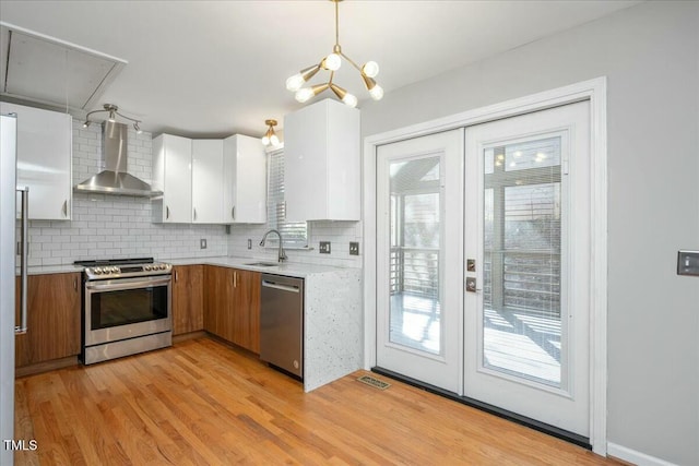 kitchen featuring wall chimney exhaust hood, sink, white cabinetry, hanging light fixtures, and appliances with stainless steel finishes