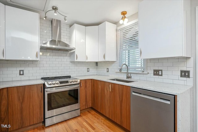 kitchen with wall chimney range hood, stainless steel appliances, sink, and white cabinets