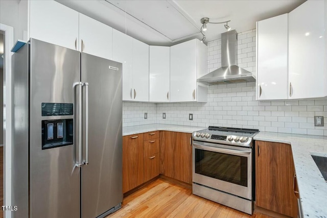 kitchen with white cabinetry, stainless steel appliances, light stone counters, decorative backsplash, and wall chimney exhaust hood