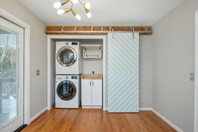 laundry room featuring stacked washer and dryer, cabinets, a chandelier, and light hardwood / wood-style flooring