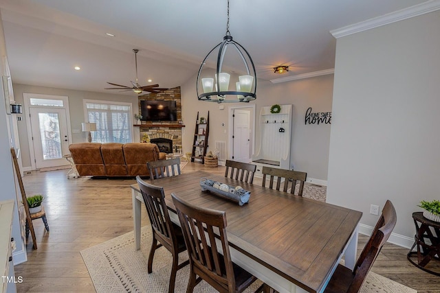 dining space featuring crown molding, a fireplace, ceiling fan with notable chandelier, and light wood-type flooring