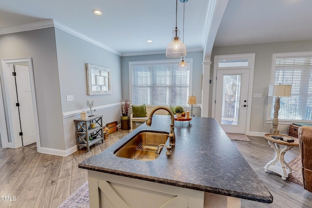 kitchen with ornamental molding, sink, hanging light fixtures, and light hardwood / wood-style flooring